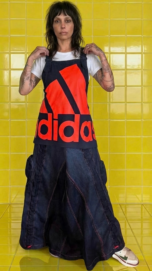 A one-of-a-kind reworked Adidas denim pinafore dress, created from quality vintage denim jeans and a vibrant neon orange Adidas logo tee.